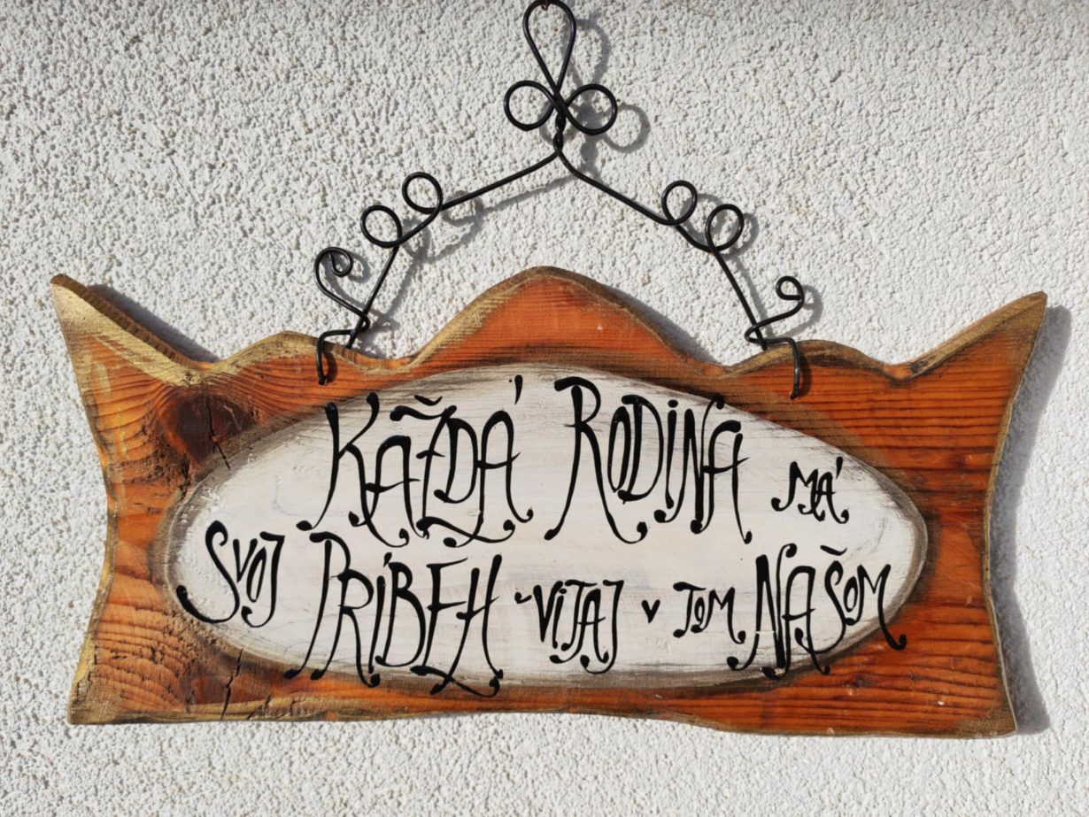 Drevený nápis s nápisom "Každá rodina má svoj príbeh" na dvere, symbolizujúci rodinné hodnoty a jedinečný príbeh každej rodiny.