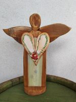Drevený anjel strážny srdca a malým dievčatkom, symbol ochrany a lásky v domove. Ručne vyrezávaný a dekoratívny, vhodný ako darček alebo ozdoba.
