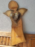 Drevený anjel s kovovým srdcom na stene, dekoratívny doplnok do interiéru alebo exteriéru.
