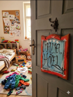 Detská izba s nápisom "Mama hotel" na dverách, plná hračiek, oblečenia a detských dekorácií, vytvára útulné a hravé prostredie pre deti.