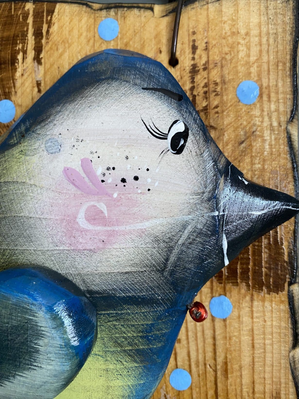 Ručne maľovaná drevená dekorácia ryba s modrými bodkami na drevenom pozadí.